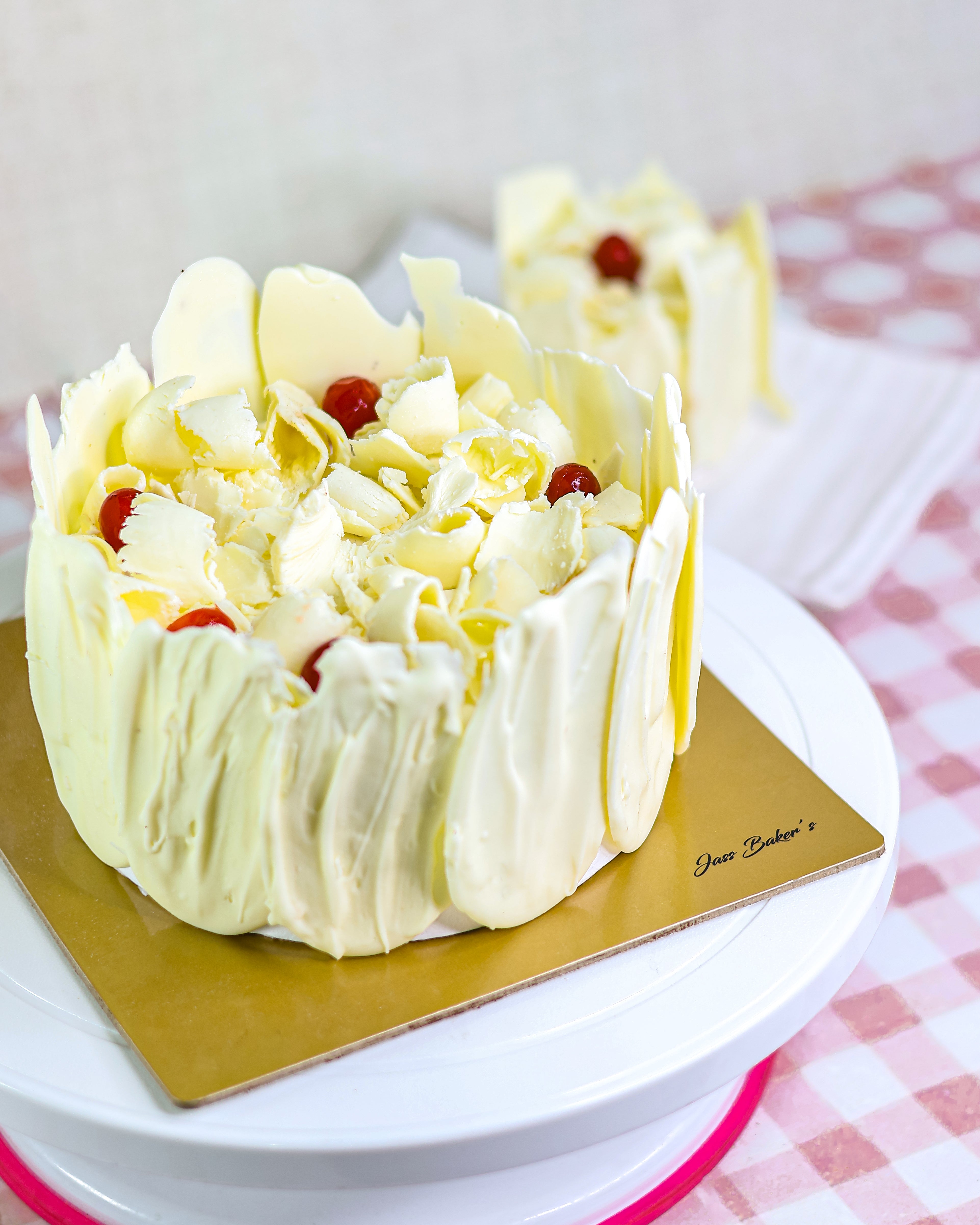 Decorative cake from Jass Baker's with white frosting and red berries on a gold cake board.